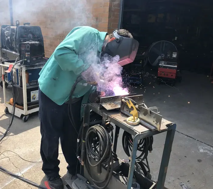 A man welding in an industrial setting with smoke coming out of the back.